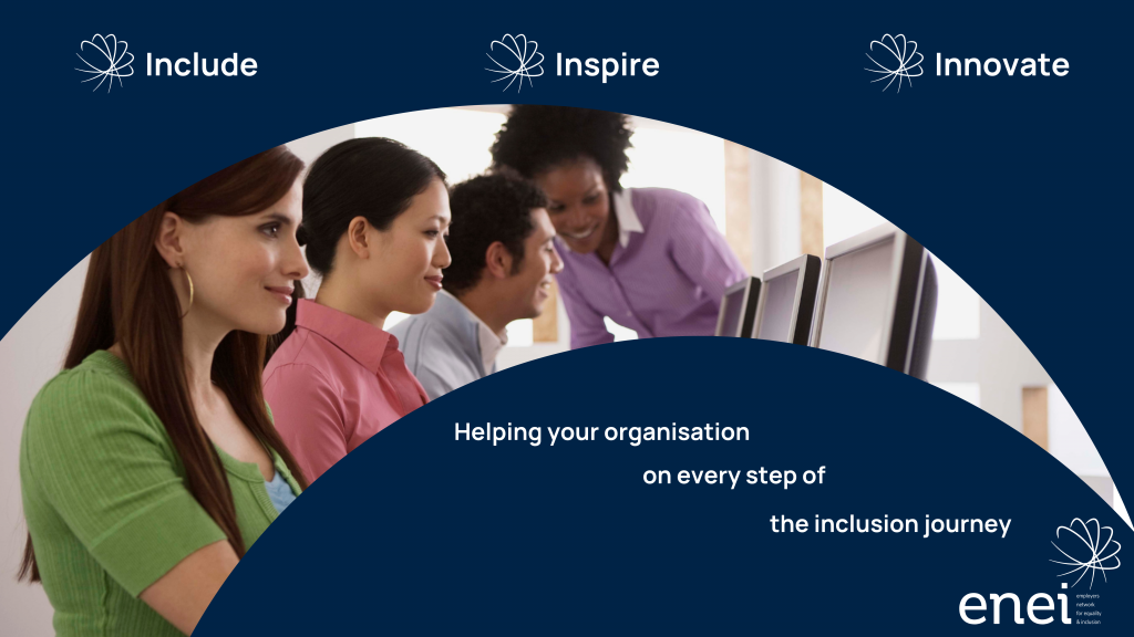 Group of ethnically diverse people sitting at a large desk with a person standing next to them, assisting them with a task.